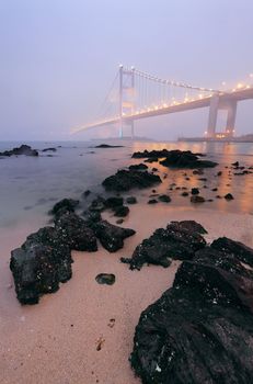 rocks on the beach and bridge in mist