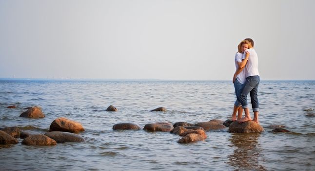 beautiful couple embrace on a stone in sea