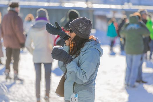 A woman trying to wear her winter gloves with her coffee in a cold winter day in the Skating Rink in Old Port of Montreal, Quebec ,Canada