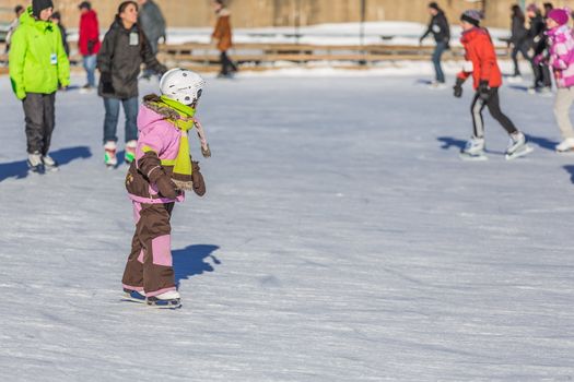  A young child is learning with joy how to ice skate in a really cold winter day in the Skating Rink in Old Port of Montreal, Quebec, Canada