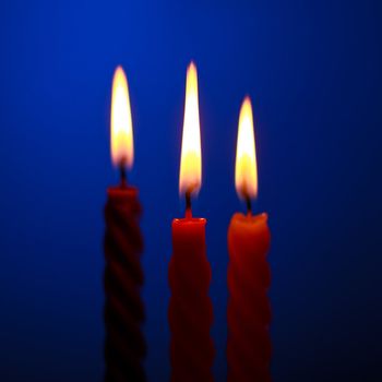 three twisted burning candles over blue background