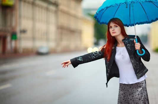 redhead girls with umbrella hitch-hiking at rainy day