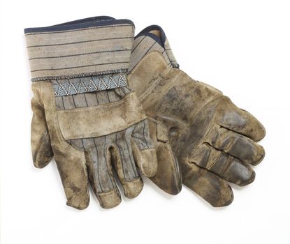 A dirty and well-worn pair of canvas and leather work gloves on white background. 