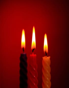 three twisted burning candles over red background