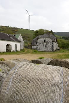 windmill above abandoned farm on lush irish countryside landscape in glenough county tipperary ireland with old round bales in foreground