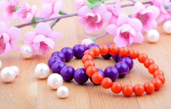 multi color coral bangles and artificial pearls, with pink flower on wooden background