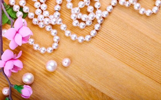 artificial pearls and pink flower on wooden background. with room for text