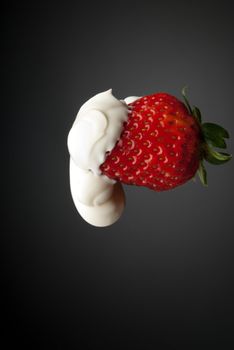 Cream youghurt over red strawberry isolated on gray side lighting