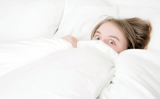 young woman looking from under the covers