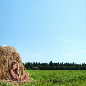 portrait of a girl next to a stack of hay under the blue sky