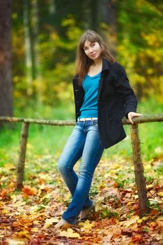 beautiful girl sitting on fence in autumn park