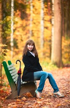 beautiful girl with umbrella sitting on bench in autumn park
