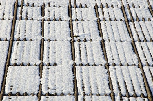 Background of slate roof covered with snow in winter sun illuminated. Material harmful to health.