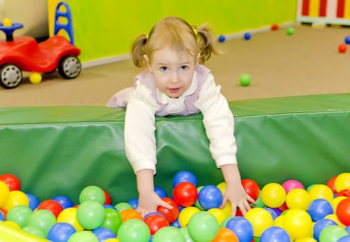 Little cute girl in playroom with colourful balls
