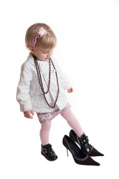 Little girl wearing mothers shoes and jewelry over white