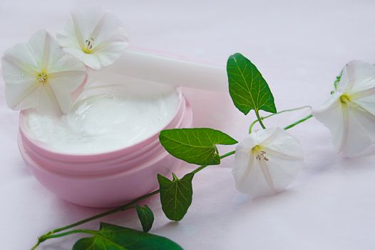 Jar of moisturizing facial cream with flower over pink