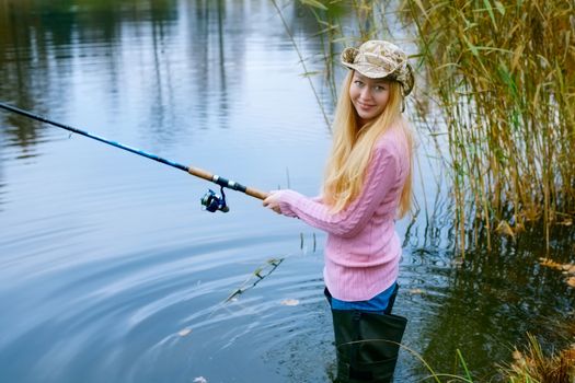 beautiful blond girl fishing in pond at autumn