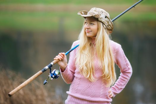 beautiful blond girl fishing in pond at autumn