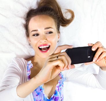 Pretty woman lying on the bed holding her smartphone