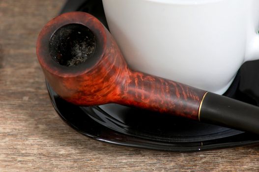 An image of pipe and white cup on saucer