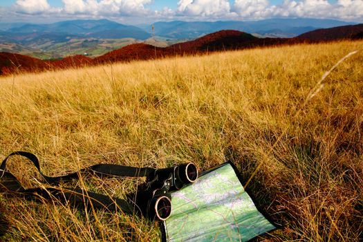 An image of binoculars and map on dry grass. Adventure theme