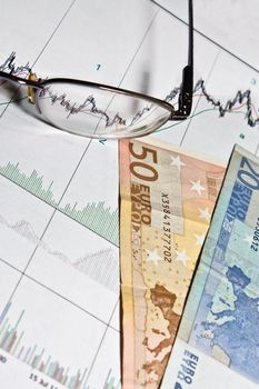 Glasses and money on graph of charts.