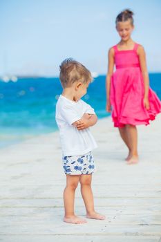 Cute toddler boy with his sister walking on jetty with turquoise sea