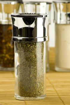 dry marjoram leaves in a glass jar on different spices background over wooden mat