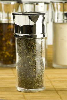 dry basil in a glass jar on different spices background over wooden mat