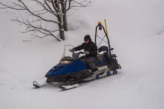 Snow mobile rider driving along skiing piste with his skidoo during snowfall in Montafon, Austria
