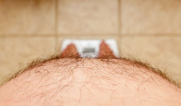 Close up of stomach of large hairy man standing on bathroom scales