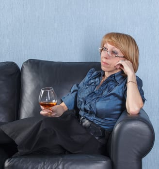 Portrait of relaxed middle aged woman with a glass brandy on couch