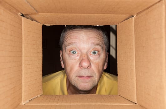 Senior caucasian man looking directly into a cardboard box and being worried