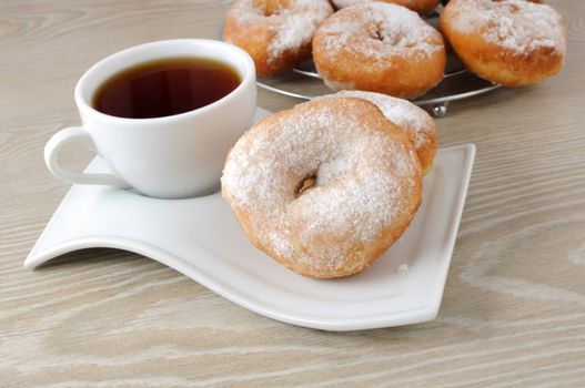 A cup of coffee and donuts in powdered sugar on a plate