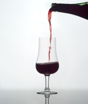Pouring red wine in a glass on white background