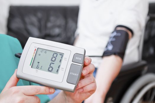 Young man having blood pressure check at home. He is in wheelchair.