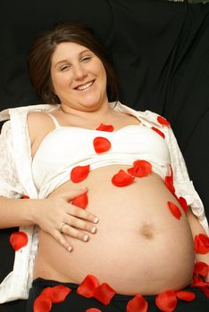 An expecting mother is showered in red rose petals while relaxing on her back.