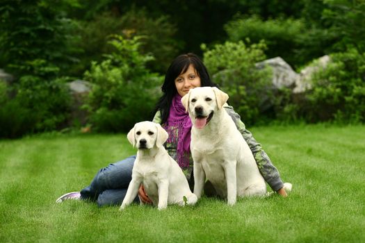 The girl sits on a green grass with two white dogs