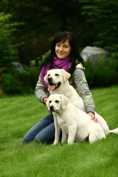 The girl sits on a green grass with two white dogs