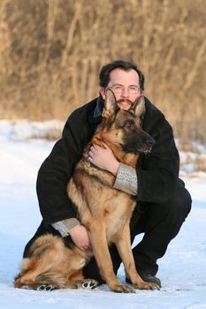 The young man wearing spectacles embraces a German shepherd dog