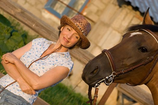 Woman in hat staying above brown horse