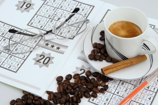 Cup of coffee with coffee beans and eyeglasses upon a book of Sudoku