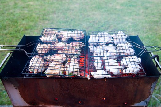 A barbeque grilling chicken meat in a summer garden.