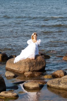 Beautiful young woman sitting on the stone on the seashore 