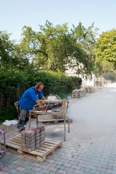 worker with circular saw sawing bricks for new street