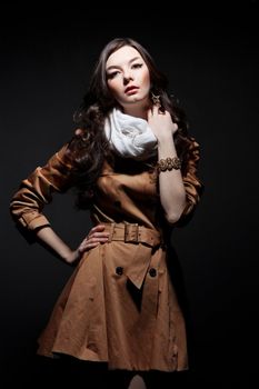 Expressive fashion studio shot of young and beautiful woman wearing brown overcoat on dark background. (Professional makeup and hair style).