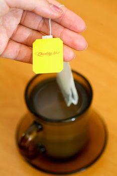 Womans hand holding tea bag on background of cup of tea