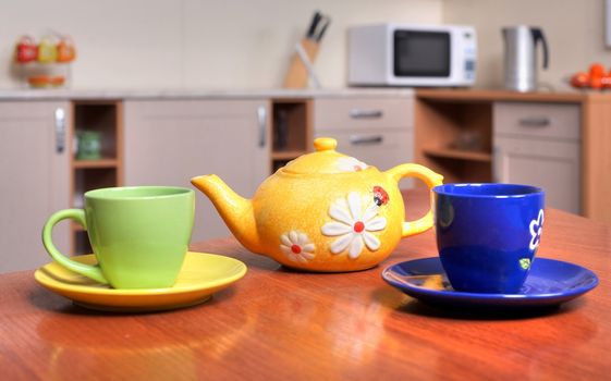 An image of yellow teapot and green and blue teacups