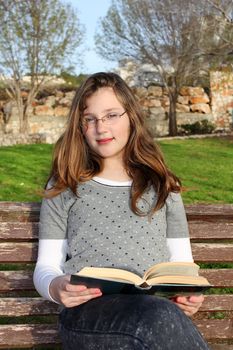 young girl with glasses, sitting in the park and reading a book