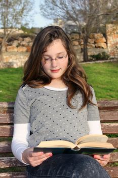 young girl with glasses, sitting in the park and reading a book